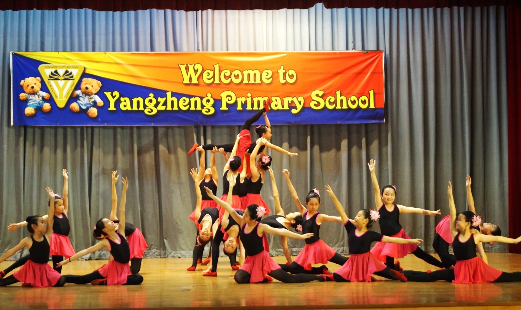 Girls in black and pink costumes perform an acrobatic dance on stage at Yangzheng Primary School.